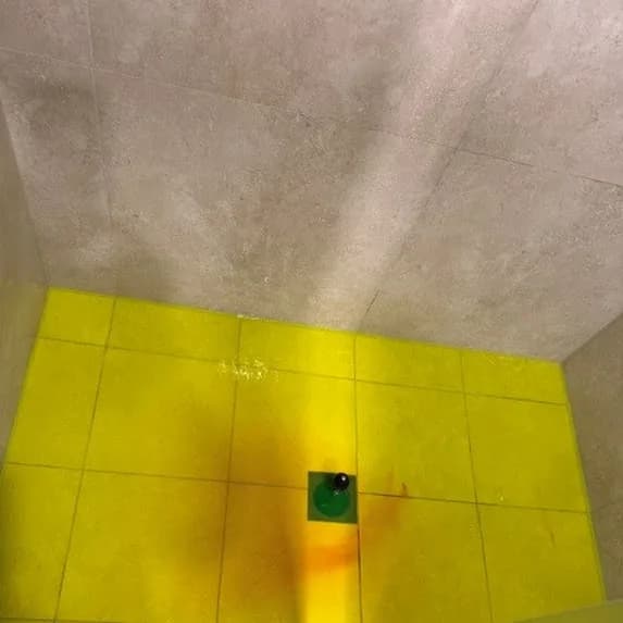Fluorescent dye tracing a leak across a shower floor, pooled around the waste