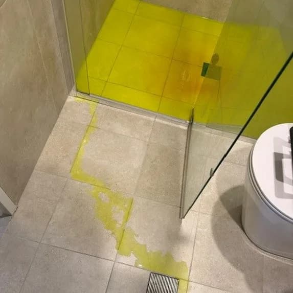 Fluorescent dye running across shower floor tiles towards the drain during a leak test