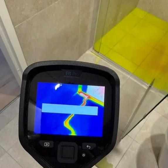 FLIR thermal imaging camera reading the heat path of a concealed leak, dye visible on the floor behind