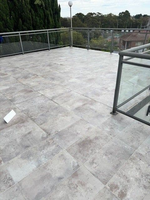 Sealed rooftop balcony in travertine-look tiles with a glass balustrade