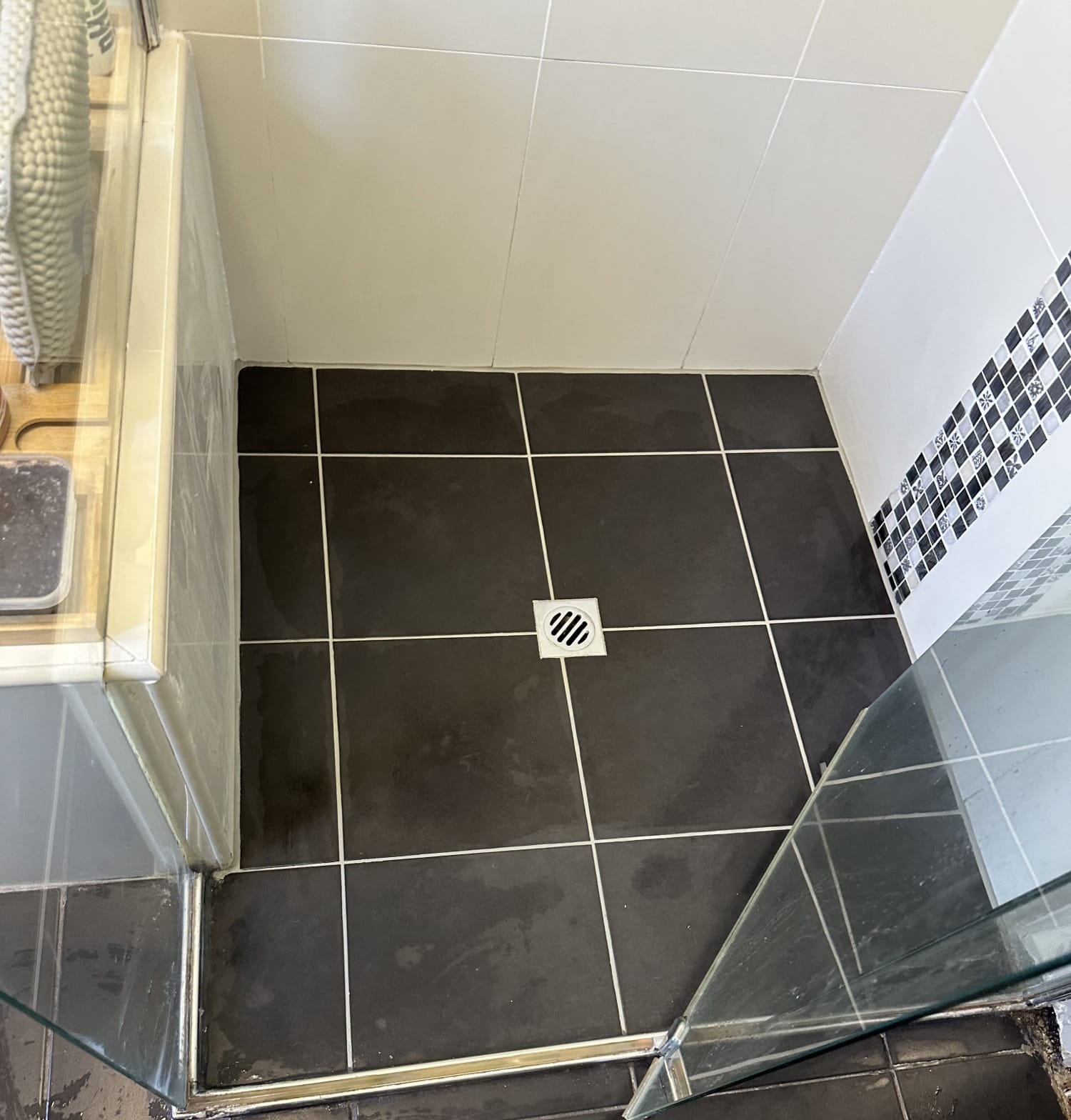 Black tiled shower floor with central drain and glass shower screen