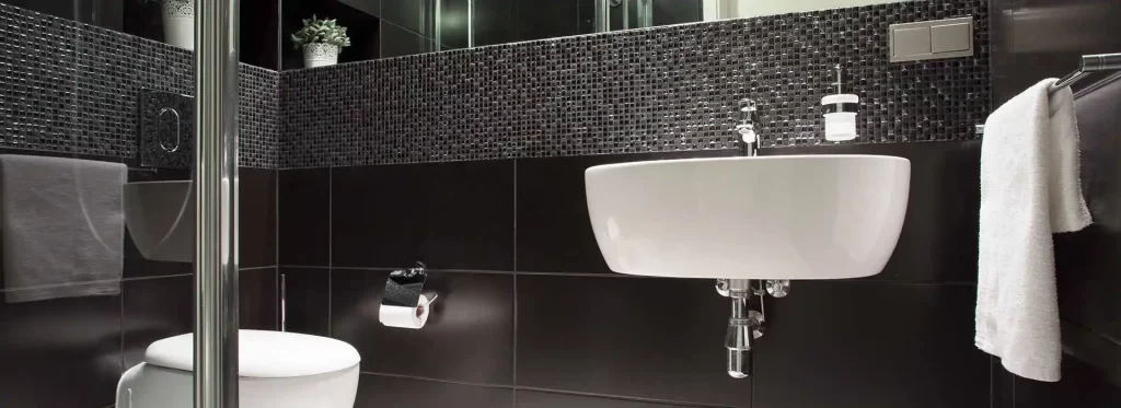 modern black-tiled bathroom with wall-mounted sink, toilet, and chrome fixtures